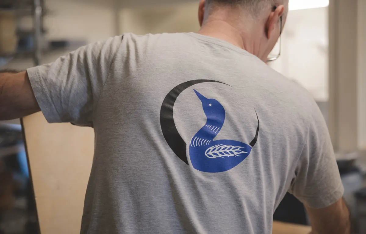 A Blue Loon baker in a loon logo T-shirt, seen from behind, working in the kitchen