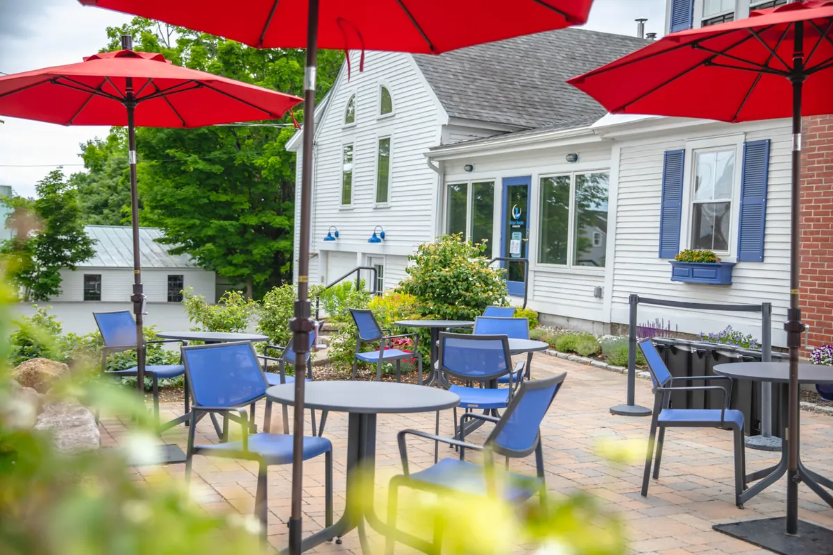 The patio with blue chairs and red umbrellas beside the white clapboard bakery