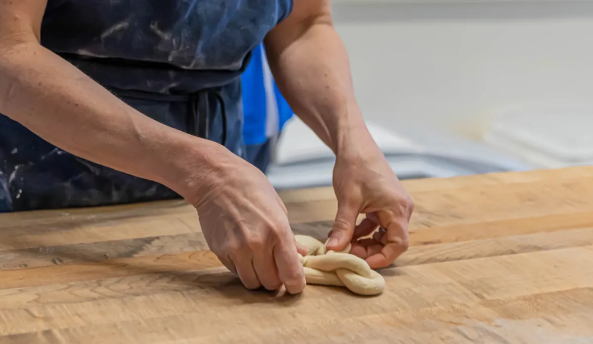 A baker shaping dough by hand on a wooden bench